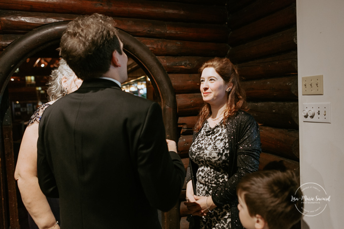 Winter wedding photos in the snow. Indoor ceremony in wooden cabin by the fire place wooden walls harsh light natural light. Wedding guests talking and laughing before ceremony. Mariage féerique hivernal à l'Hôtel Mont-Gabriel. Mariage hiver Laurentides. Photographe mariage Montréal | Lisa-Marie Savard Photographie | Montréal, Québec | www.lisamariesavard.com