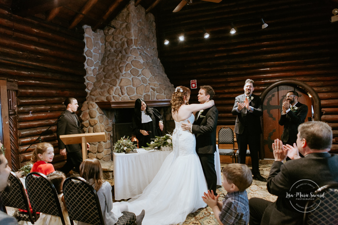 Winter wedding photos in the snow. Indoor ceremony in wooden cabin by the fire place wooden walls harsh light natural light. Bride and groom first kiss during ceremony. Mariage féerique hivernal à l'Hôtel Mont-Gabriel. Mariage hiver Laurentides. Photographe mariage Montréal | Lisa-Marie Savard Photographie | Montréal, Québec | www.lisamariesavard.com