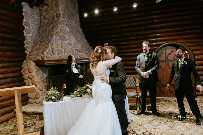 Winter wedding photos in the snow. Indoor ceremony in wooden cabin by the fire place wooden walls harsh light natural light. Bride and groom first kiss during ceremony. Mariage féerique hivernal à l'Hôtel Mont-Gabriel. Mariage hiver Laurentides. Photographe mariage Montréal | Lisa-Marie Savard Photographie | Montréal, Québec | www.lisamariesavard.com