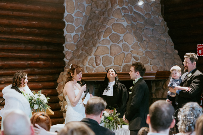 Winter wedding photos in the snow. Indoor ceremony in wooden cabin by the fire place wooden walls harsh light natural light. Bride and groom exchanging vows during ceremony. Mariage féerique hivernal à l'Hôtel Mont-Gabriel. Mariage hiver Laurentides. Photographe mariage Montréal | Lisa-Marie Savard Photographie | Montréal, Québec | www.lisamariesavard.com