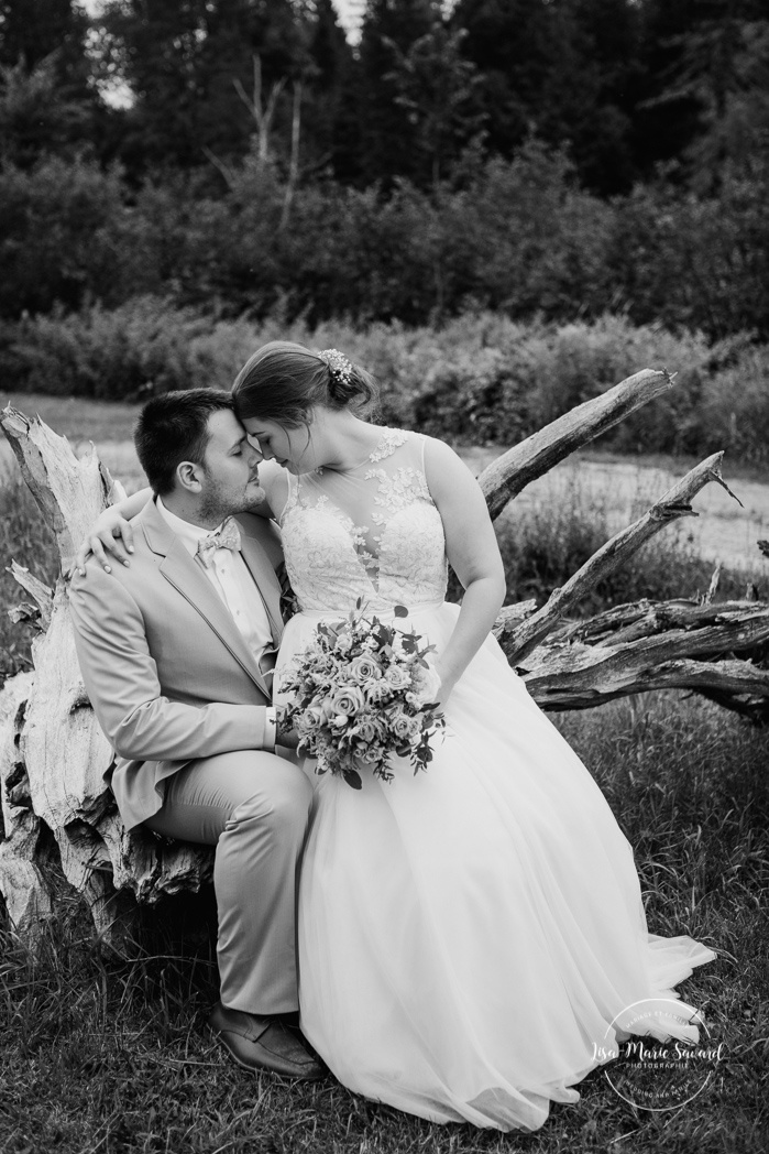 Bride and groom sitting on large drift wood. Photos de mariage rustique à la campagne. Photographe de mariage à Trois-Rivières