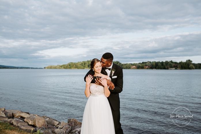 Bride and groom kissing by the river. African American groom and Caucasian bride. Mariage en Outaouais. Fairmont Le Château Montebello outdoor wedding. Ottawa photographer.