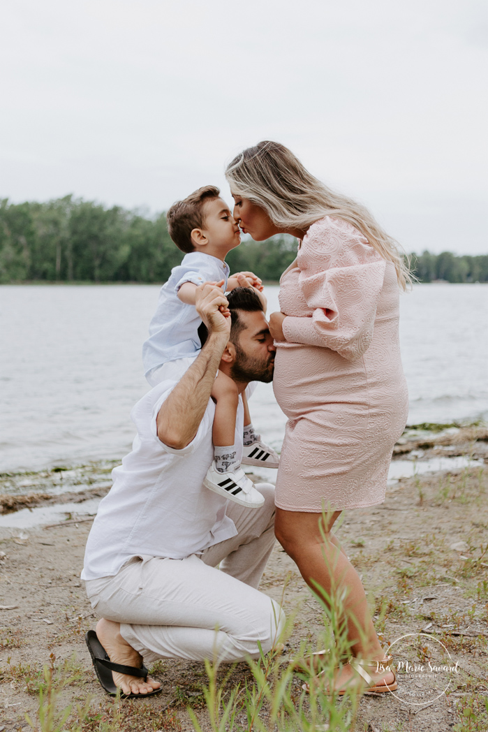 Mom kissing toddler, dad kissing belly. Maternity photos next to river. Maternity session by waterfront. Maternity photos with toddler. Maternity session little boy. Séance maternité à Laval. Photographe de maternité à Laval. Laval maternity photographer.