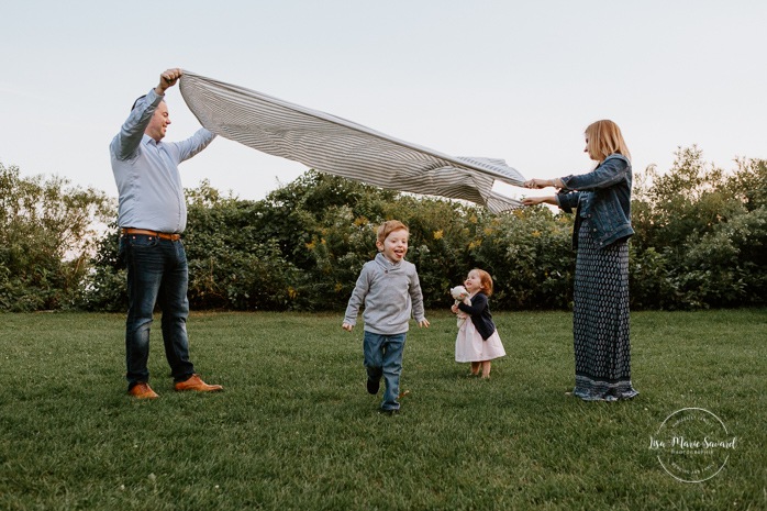 Children running under blanket. Children playing with blanket. Outdoor family session. Outdoor family photos. Family of four photos. Family photos with dog. Photos de famille dans les West Island à Montréal. Photographe de famille à Montréal. Montreal West Island family photos. Montreal family photographer.