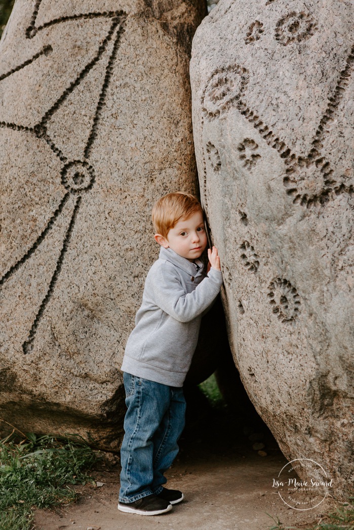 Shy boy hiding behind rocks. Toddler boy portrait. Outdoor family session. Outdoor family photos. Family of four photos. Photographe à Dorval. Photographe de famille à Montréal. Montreal West Island family photos. Montreal family photographer.