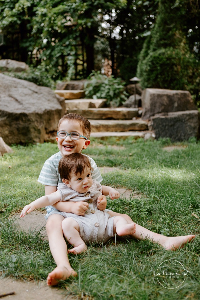 Toddler boy holding baby brother. Sibling photos with boys. In-home family session. Lifestyle family photos. Back yard family photos. Family photos with two boys. Séance photo à Montréal. Séance familiale à Montréal. Town of Mount Royal family photographer