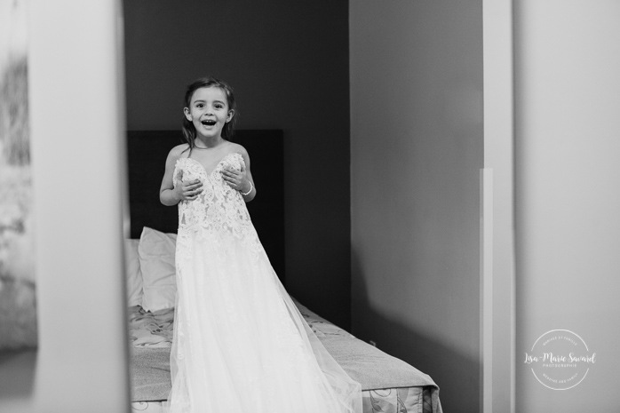 Flower girl trying on bride's wedding dress. Bride getting ready with bridesmaids in hotel room. Pandemic wedding. COVID-19 micro wedding. Mariage en Beauce durant la pandémie. Photographe de mariage Beauce. Motel Invitation Sainte-Marie.