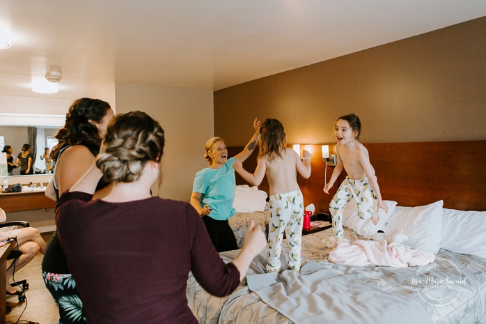 Flower girls jumping on bed. Bride getting ready with bridesmaids in hotel room. Pandemic wedding. COVID-19 micro wedding. Mariage en Beauce durant la pandémie. Photographe de mariage Beauce. Motel Invitation Sainte-Marie.