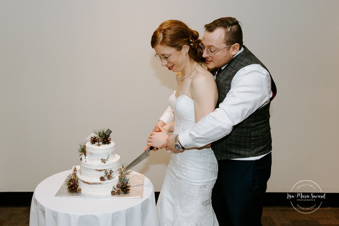 Bride and groom cutting cake. Wedding reception in dark venue. Intimate wedding reception. Mariage à Chicoutimi en hiver. Photographe de mariage au Saguenay. Mariage Hôtel Chicoutimi