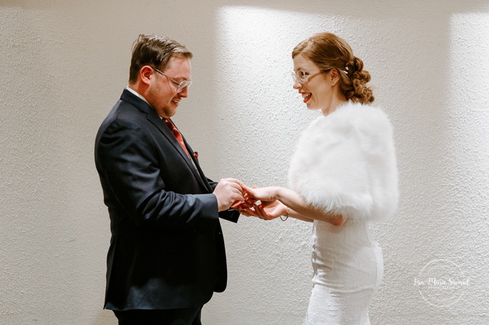 Bride and groom exchanging rings. Intimate hotel wedding ceremony. Wedding ceremony in dark hall with artificial light. Mariage à Chicoutimi en hiver. Photographe de mariage au Saguenay. Mariage Hôtel Chicoutimi.
