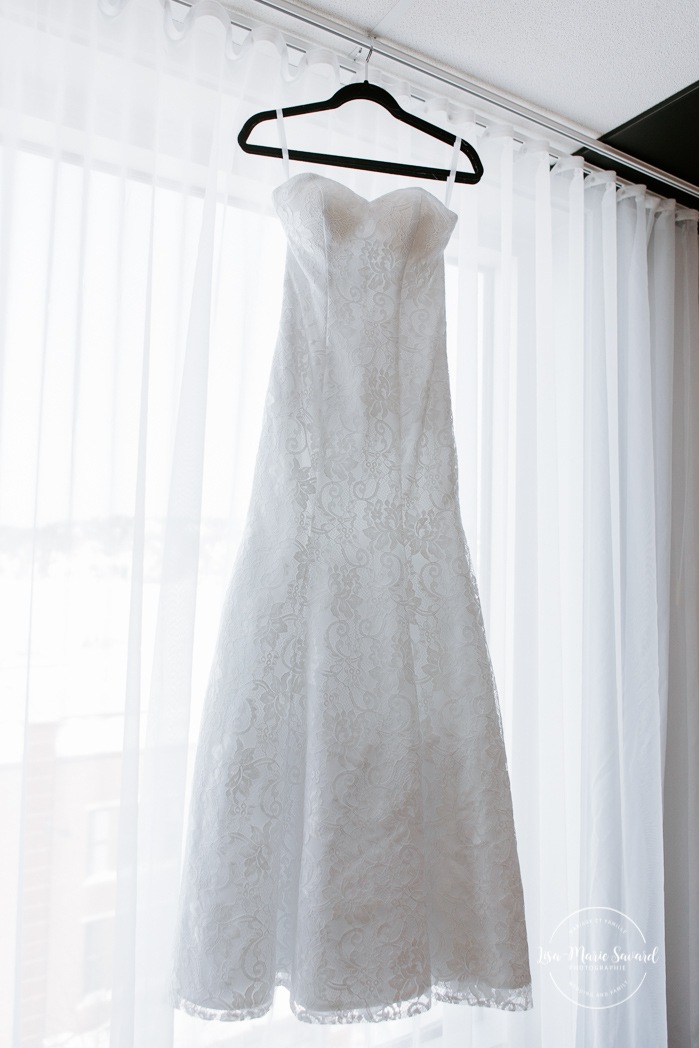 Wedding dress hanging in front of window. Mariage à Chicoutimi en hiver. Mariage Hôtel Chicoutimi. Photographe de mariage au Saguenay.