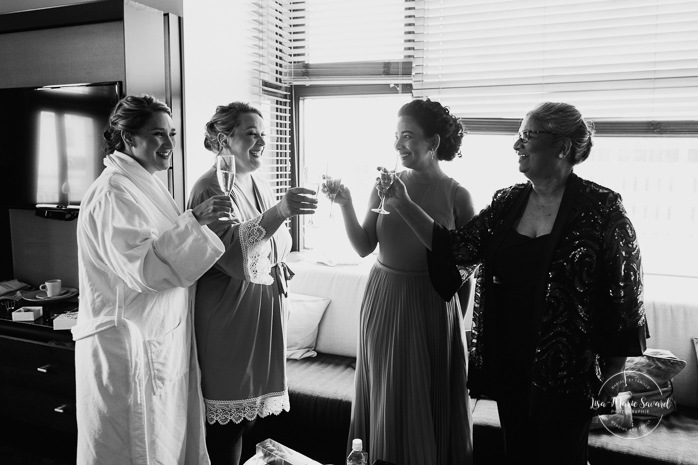Bride popping bottle of champagne. Bride getting ready with bridesmaids in hotel room. Hôtel Le Germain Québec. Mariage dans le Vieux-Québec. Photographe mariage Québec. Old Quebec wedding photos.