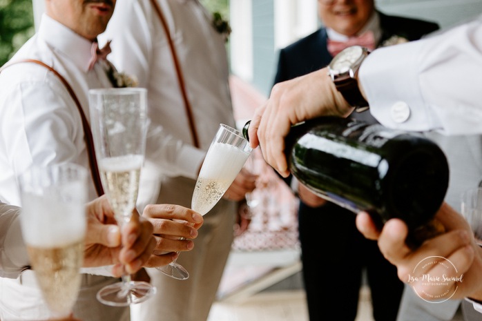 Groom popping champagne with groomsmen. Photographe de mariage en Mauricie. Mariage Le Baluchon Éco-Villégiature. 