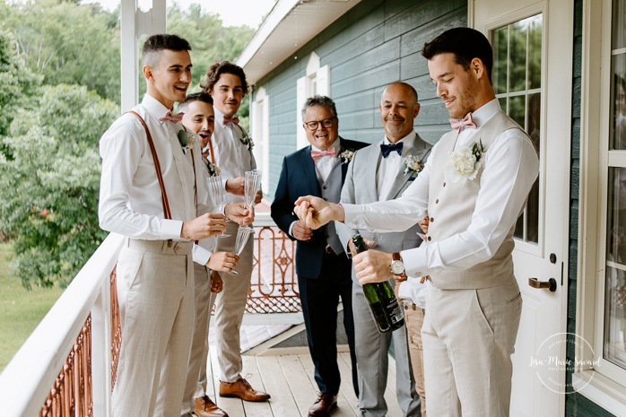 Groom popping champagne with groomsmen. Photographe de mariage en Mauricie. Mariage Le Baluchon Éco-Villégiature. 