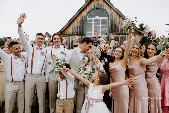 Wedding group photo in front of wooden chapel. Photographe de mariage en Mauricie. Mariage Le Baluchon Éco-Villégiature. 