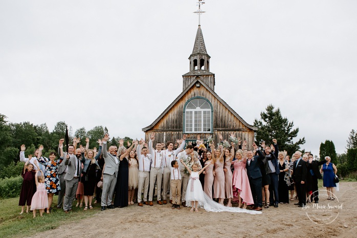 Wedding group photo in front of wooden chapel. Photographe de mariage en Mauricie. Mariage Le Baluchon Éco-Villégiature. 