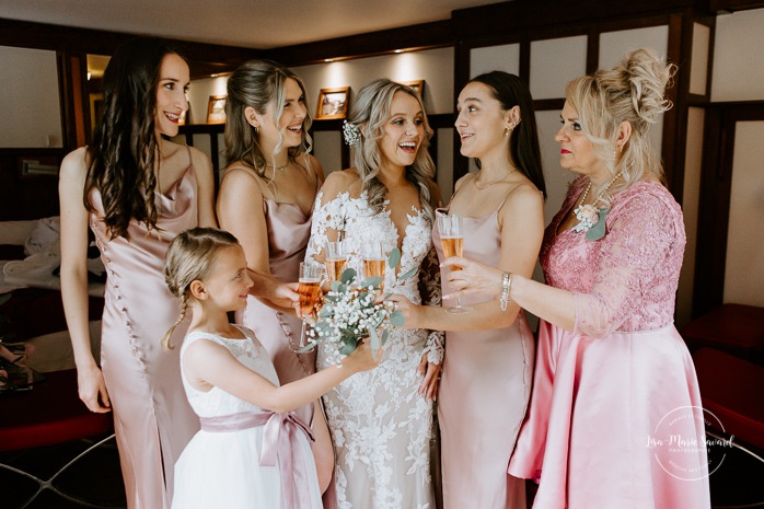 Bride popping bottle of champagne with bridesmaids. Bride getting ready with bridesmaids in hotel room. Photographe de mariage en Mauricie. Mariage Le Baluchon Éco-Villégiature. 