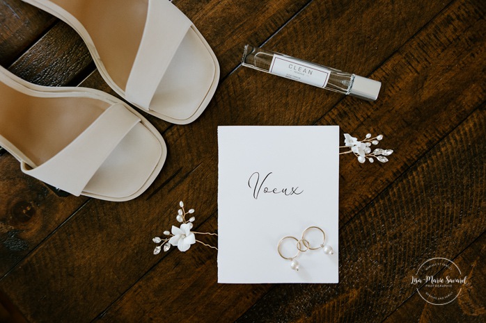 Wedding flat lay high heels perfume hair accessories earrings and vow booklet. Bride getting with bridesmaids and family at home. Mariage à la Cabane à sucre Constantin. Photographe de mariage à Montréal. Cabane à sucre Constantin wedding. Montreal wedding photographer.