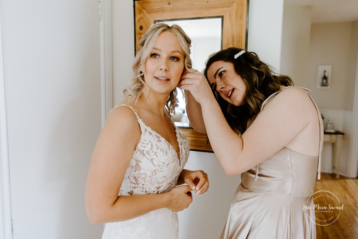 Bridesmaid helping bride put earring on. Bride getting with bridesmaids and family at home. Mariage à la Cabane à sucre Constantin. Photographe de mariage à Montréal. Cabane à sucre Constantin wedding. Montreal wedding photographer.