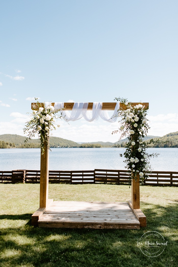 Wooden arch with floral arrangement Lakefront wedding ceremony. Outdoor wedding ceremony in front of lake. Photographe de mariage à Mont-Tremblant. Mariage Le Grand Lodge Mont-Tremblant. Mont-Tremblant wedding photographer. Tremblant wedding photos.