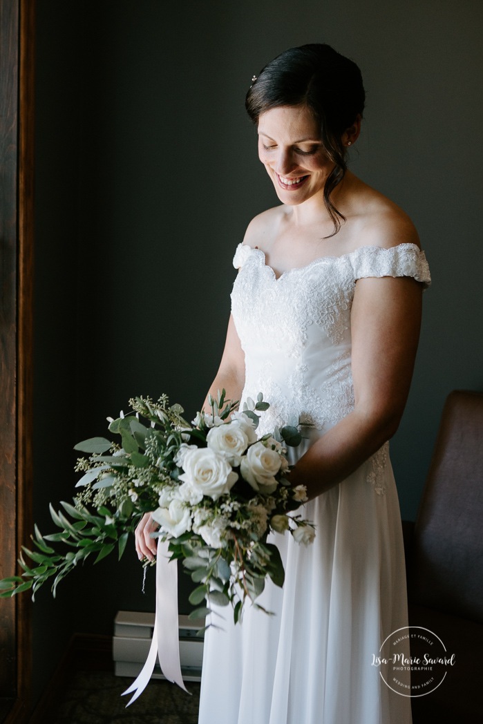 Bride looking at bouquet in front of window. Photographe de mariage à Mont-Tremblant. Mariage Le Grand Lodge Mont-Tremblant. Mont-Tremblant wedding photographer. Tremblant wedding photos.