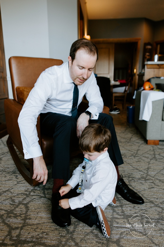 Groom getting ready with toddler son and family in hotel room. Photographe de mariage à Mont-Tremblant. Mariage Le Grand Lodge Mont-Tremblant. Mont-Tremblant wedding photographer. Tremblant wedding photos.