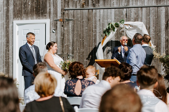 Outdoor wedding ceremony on front of barn. Barn wedding ceremony. Photographe de mariage au Lac-Saint-Jean. Photographe mariage Saguenay. Mariage à L'Orée des Champs Saint-Nazaire.