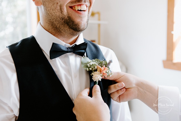 Groomsman helping groom put on boutonniere. Photographe de mariage au Lac-Saint-Jean. Photographe mariage Saguenay. Mariage à L'Orée des Champs Saint-Nazaire.