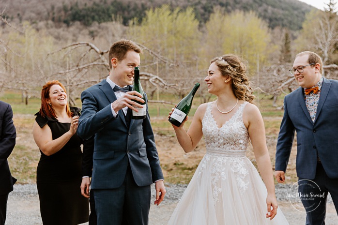 Bride and groom popping champagne with bridal party. Photographe mariage au Verger du Flanc Nord. Verger du Flanc Nord wedding photographer. Photographe mariage Montérégie. Photographe mariage Montréal. Monteregie wedding photographer. Montreal wedding photographer.