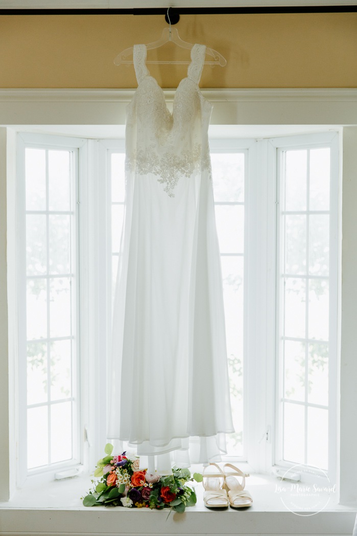 Bride's dress hanging in front of window. Photographe de mariage à Saint-Hyacinthe. Photographe St-Hyacinthe. Photos de mariage au Jardin Daniel A. Séguin.