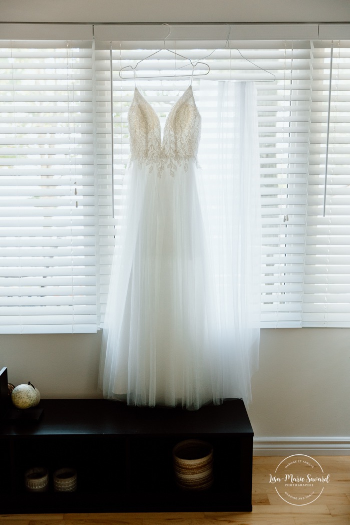 Wedding dress hanging in front of window. Mariage à la Pointe-du-Moulin. Photographe mariage à Montréal. Pointe-du-Moulin wedding. Montreal wedding photographer.