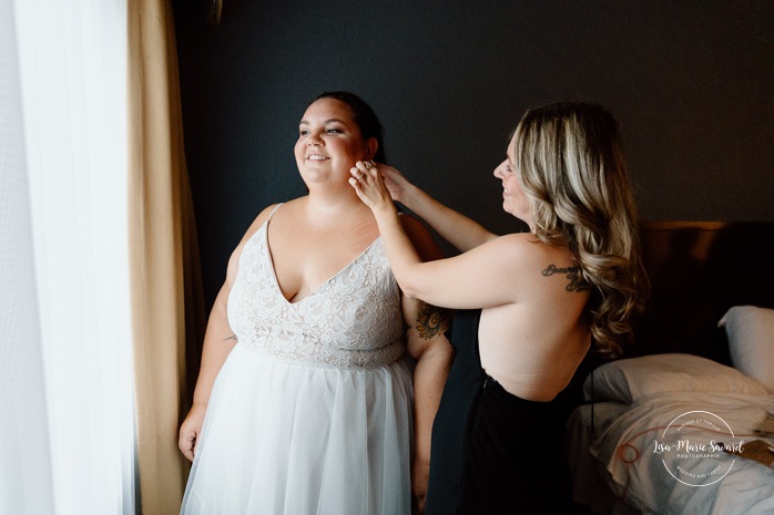 Bride getting ready in dark hotel room. Mariage avec deux femmes. Mariage LGBTQ+ au Saguenay-Lac-Saint-Jean. Photographe de mariage au Saguenay.