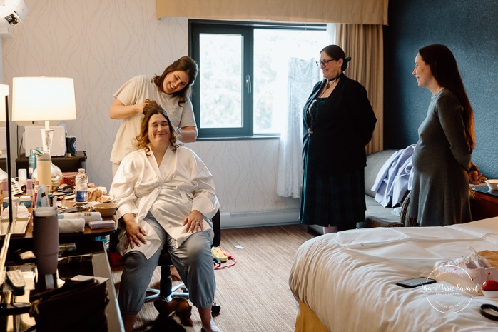 Bride getting ready in dark hotel room. Mariage avec deux femmes. Mariage LGBTQ+ au Saguenay-Lac-Saint-Jean. Photographe de mariage au Saguenay.