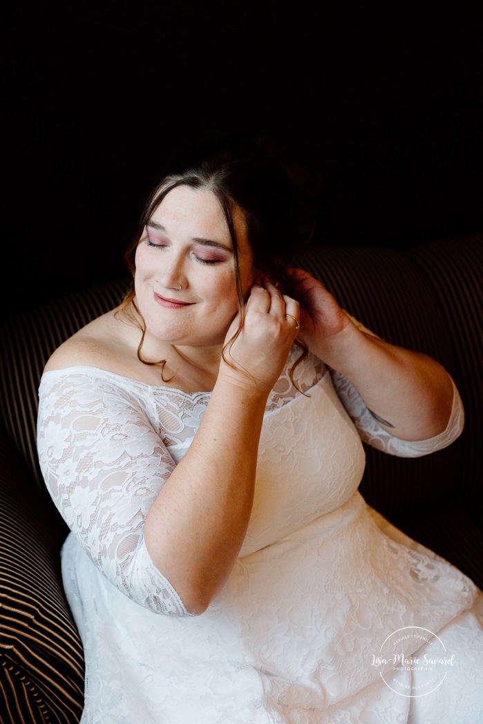 Bride getting ready in dark hotel room. Mariage avec deux femmes. Mariage LGBTQ+ au Saguenay-Lac-Saint-Jean. Photographe de mariage au Saguenay.