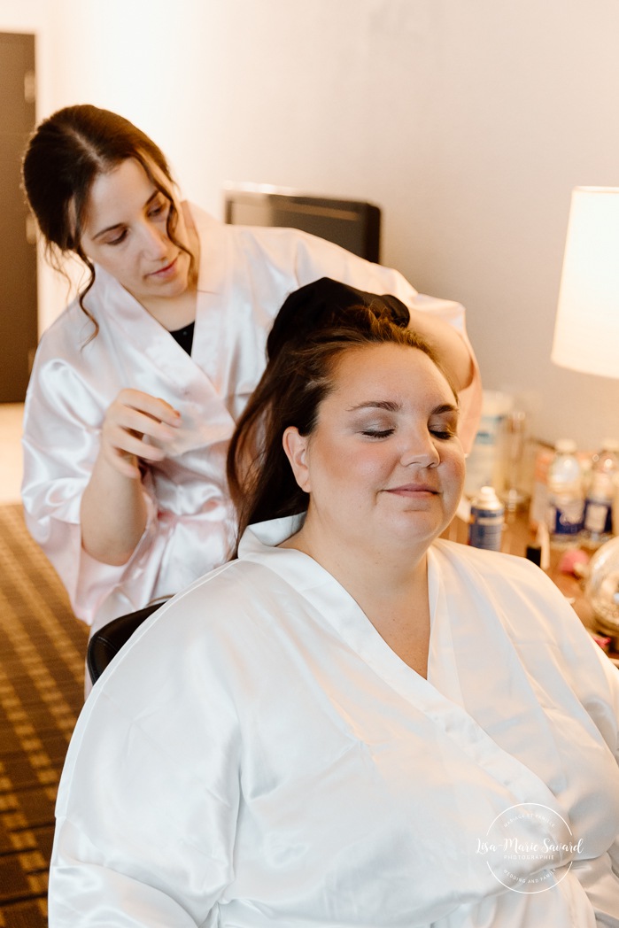 Bride getting ready in dark hotel room. Mariage avec deux femmes. Mariage LGBTQ+ au Saguenay-Lac-Saint-Jean. Photographe de mariage au Saguenay.