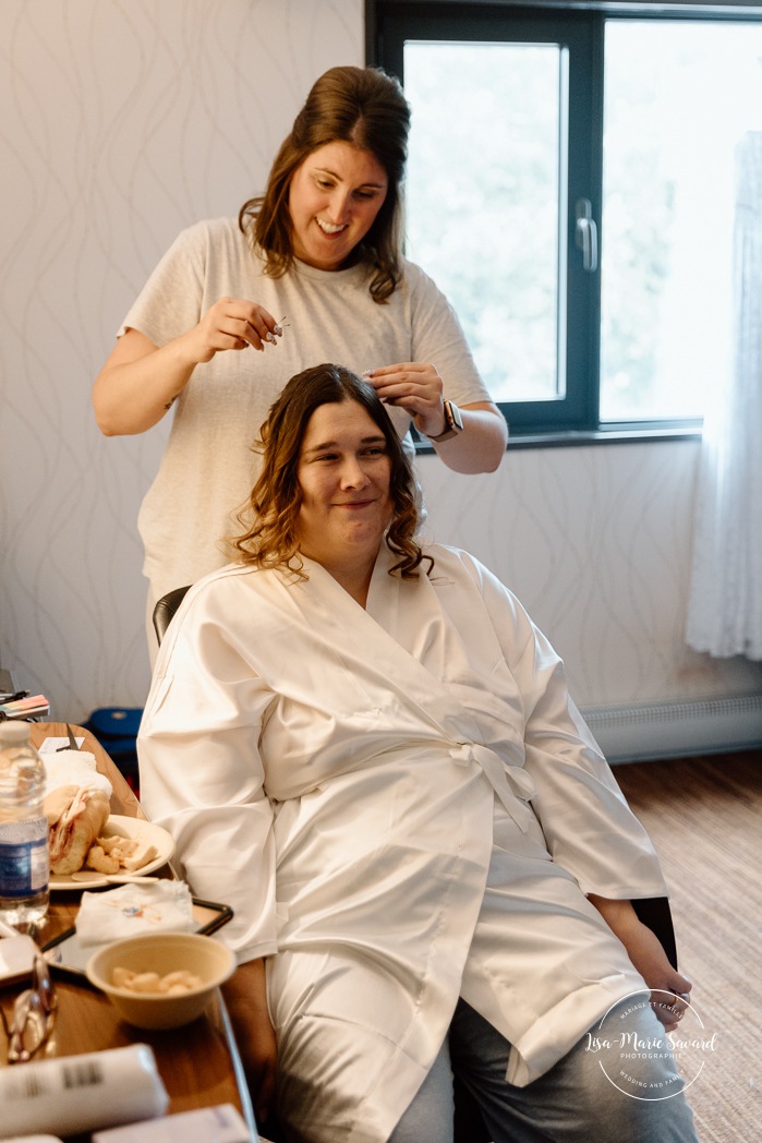 Bride getting ready in dark hotel room. Mariage avec deux femmes. Mariage LGBTQ+ au Saguenay-Lac-Saint-Jean. Photographe de mariage au Saguenay.