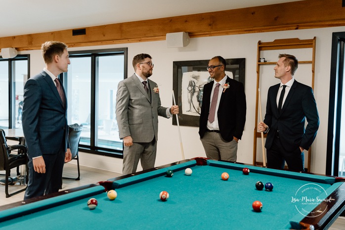 Groom playing billiards with groomsmen. Groom getting ready with family in hotel room. Mariage à l'Auberge des Îles au Lac-Saint-Jean. Photographe de mariage au Saguenay-Lac-Saint-Jean.