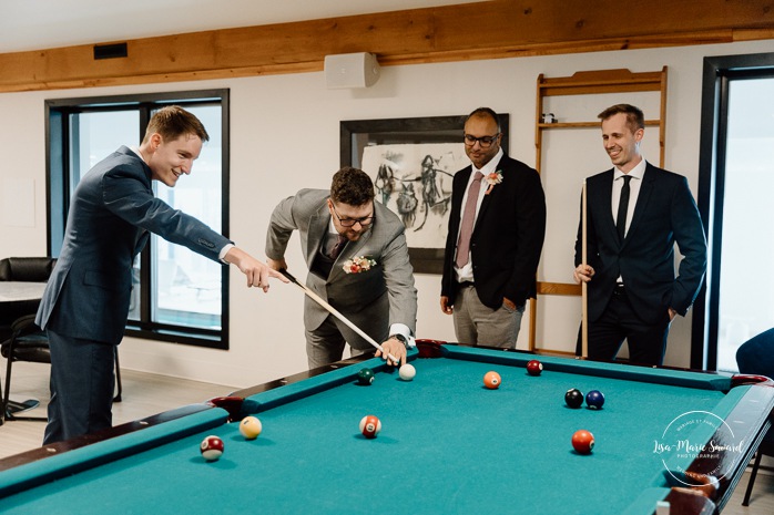 Groom playing billiards with groomsmen. Groom getting ready with family in hotel room. Mariage à l'Auberge des Îles au Lac-Saint-Jean. Photographe de mariage au Saguenay-Lac-Saint-Jean.