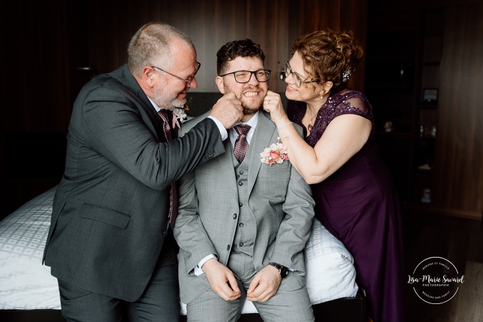 Groom getting ready with family in hotel room. Mariage à l'Auberge des Îles au Lac-Saint-Jean. Photographe de mariage au Saguenay-Lac-Saint-Jean.