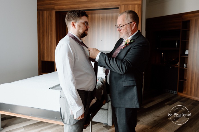 Groom getting ready with family in hotel room. Mariage à l'Auberge des Îles au Lac-Saint-Jean. Photographe de mariage au Saguenay-Lac-Saint-Jean.