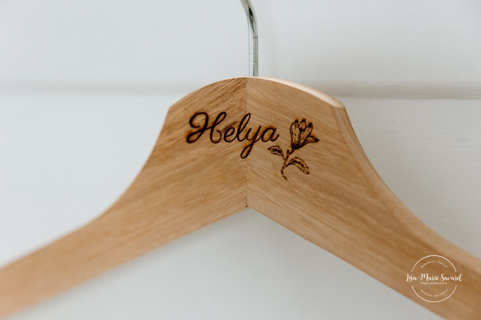 Wedding dress hanging in front of window. Bride getting ready with bridesmaids in hotel room. Mariage à l'Auberge des Îles au Lac-Saint-Jean. Photographe de mariage au Saguenay-Lac-Saint-Jean.