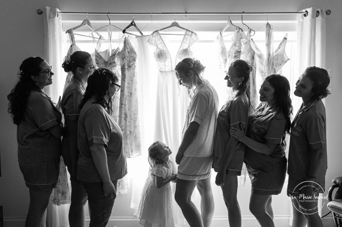 Wedding dresses hanging in front of window. Bride getting ready with bridesmaids. Mariage au bord du Lac-Saint-Jean. Auberge des Îles. Photographe mariage Saguenay-Lac-Saint-Jean