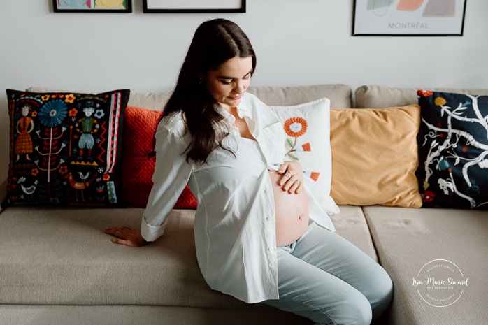 Expecting mother cradling her belly. In-home maternity photos. Living room maternity photos. Photos de maternité à la maison à Montréal. Photographe maternité Montréal. Montreal in-home maternity photos. Montreal maternity photographer.