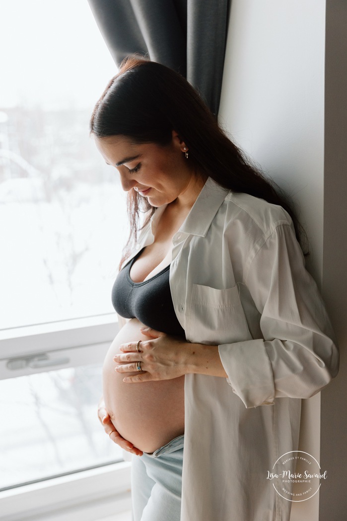 Expecting mother cradling her belly. In-home maternity photos. Bedroom maternity photos. Photos de maternité à la maison à Montréal. Photographe maternité Montréal. Montreal in-home maternity photos. Montreal maternity photographer.