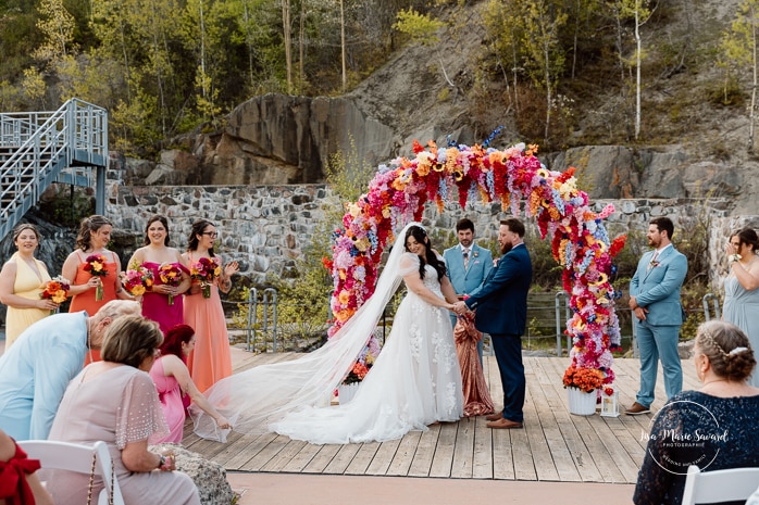 Outdoor wedding ceremony with floral arch. Colorful wedding ideas. Photographe de mariage au Saguenay. Photographe Saguenay-Lac-Saint-Jean. Mariage Pulperie de Chicoutimi. Jardin des Vestiges. Bâtiment 1912. Saguenay wedding photographer.