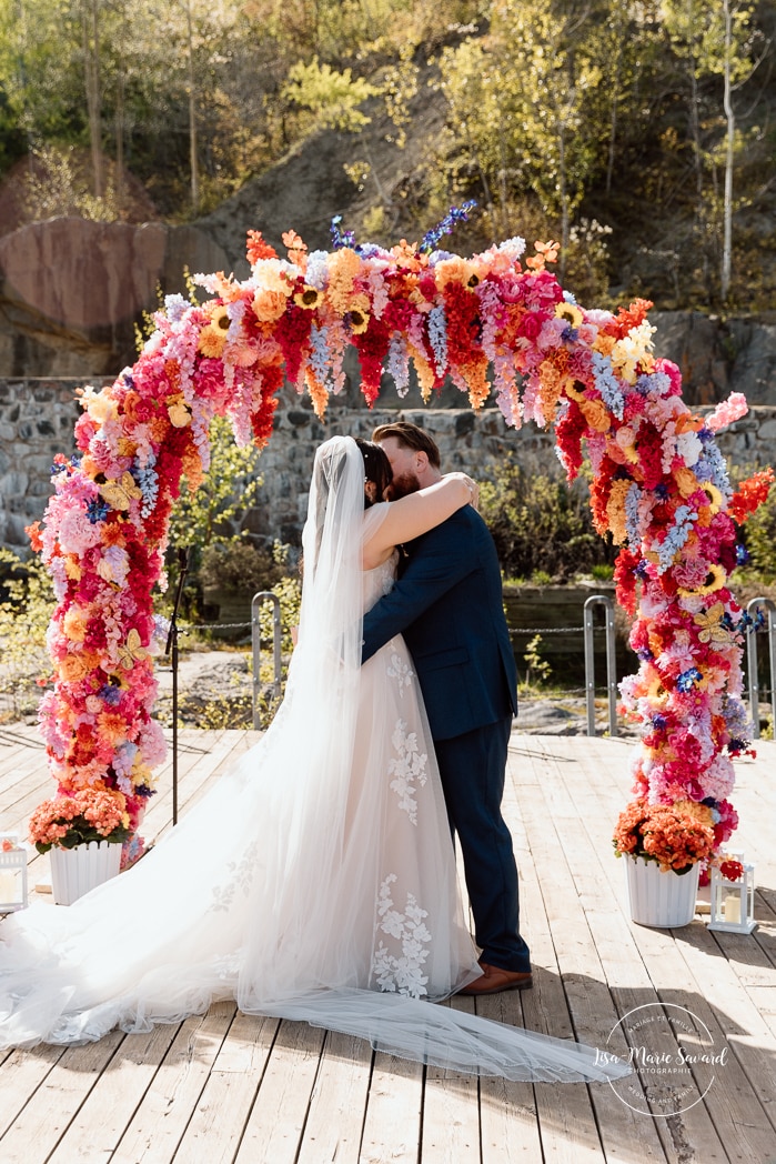 Outdoor wedding ceremony with floral arch. Colorful wedding ideas. Photographe de mariage au Saguenay. Photographe Saguenay-Lac-Saint-Jean. Mariage Pulperie de Chicoutimi. Jardin des Vestiges. Bâtiment 1912. Saguenay wedding photographer.