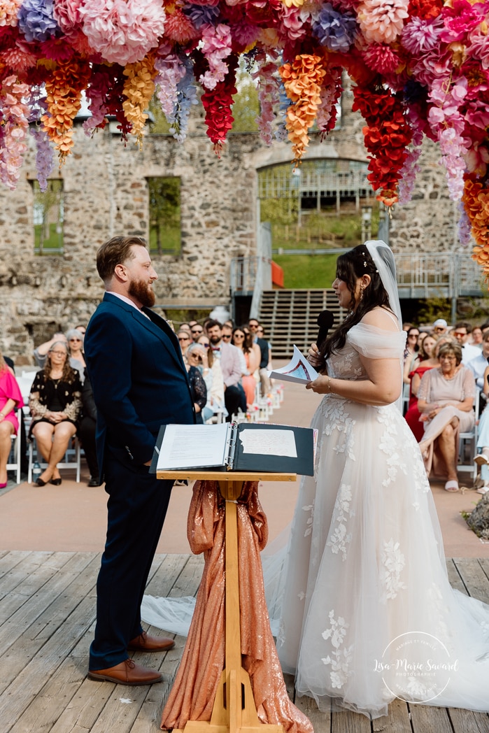 Outdoor wedding ceremony with floral arch. Colorful wedding ideas. Photographe de mariage au Saguenay. Photographe Saguenay-Lac-Saint-Jean. Mariage Pulperie de Chicoutimi. Jardin des Vestiges. Bâtiment 1912. Saguenay wedding photographer.