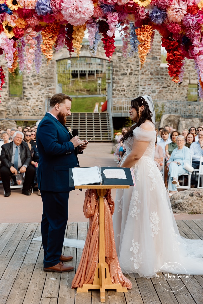Outdoor wedding ceremony with floral arch. Colorful wedding ideas. Photographe de mariage au Saguenay. Photographe Saguenay-Lac-Saint-Jean. Mariage Pulperie de Chicoutimi. Jardin des Vestiges. Bâtiment 1912. Saguenay wedding photographer.