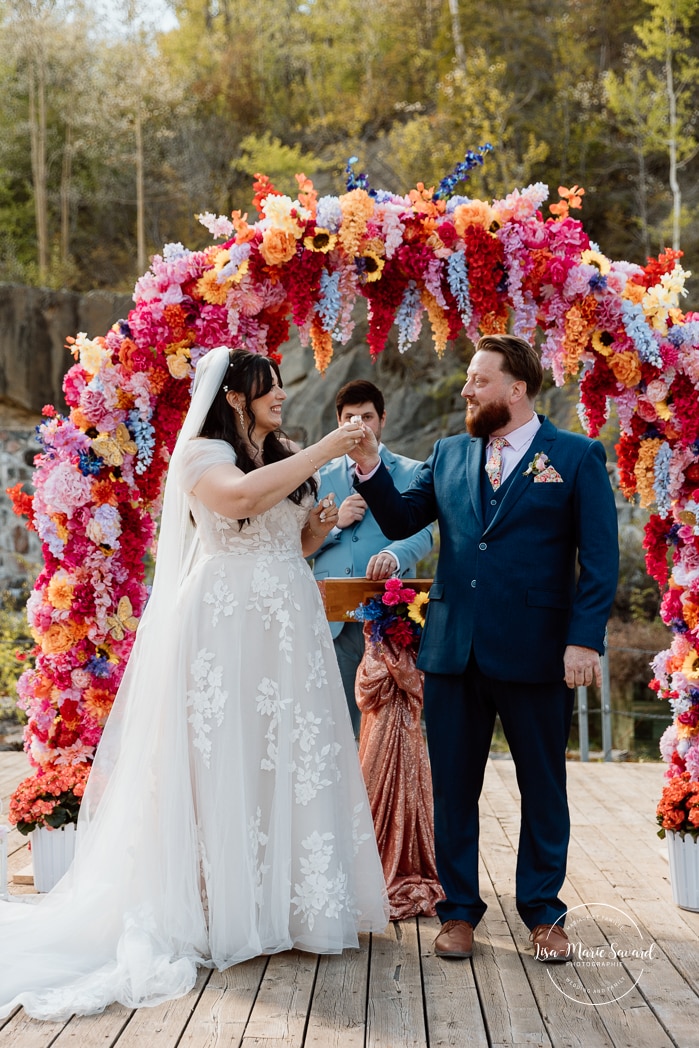 Outdoor wedding ceremony with floral arch. Colorful wedding ideas. Photographe de mariage au Saguenay. Photographe Saguenay-Lac-Saint-Jean. Mariage Pulperie de Chicoutimi. Jardin des Vestiges. Bâtiment 1912. Saguenay wedding photographer.